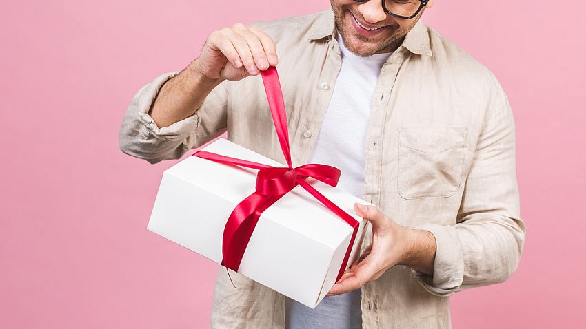 Holiday concept. Portrait of a young man opening gift box isolated over pink background. - Foto: iStock / Denis_Vermenko
