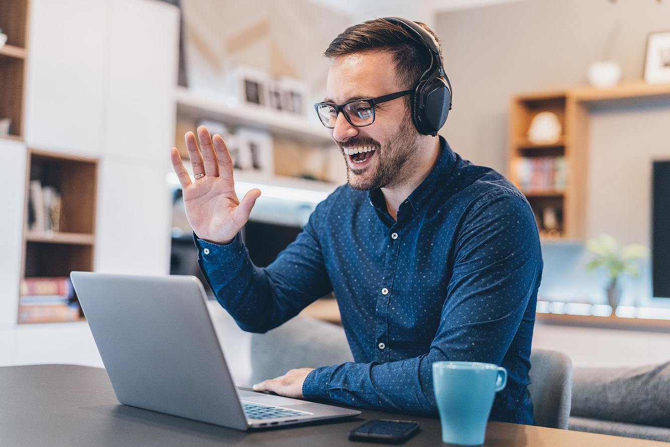 Arbeiten im Homeoffice Mann winkt im Homeoffice in Laptop-Kamera