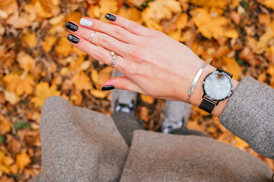 Frauenhand mit einem silbernen Armband mit Gravur und schwarzer Armbanduhr um das Handgelenk