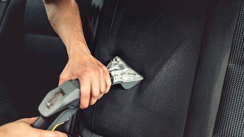 Ein Mann reinigt mit einem Autostaubsauger die Sitze - Foto: iStock/Bogdanhoda