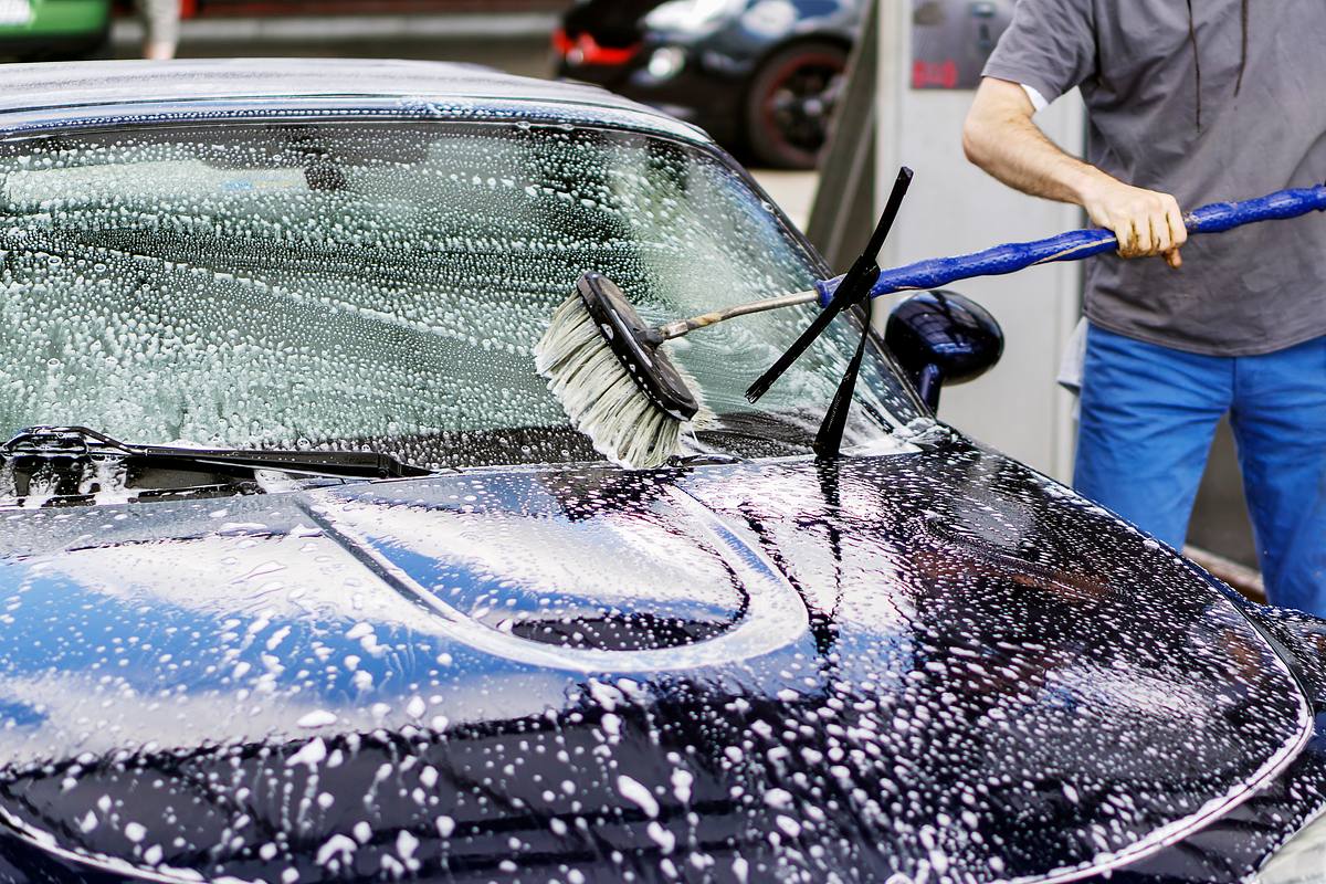 Mann putzt sein Auto mit einer Autowaschbürste