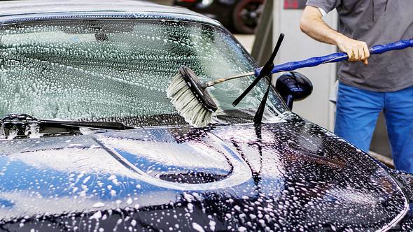 Mann putzt sein Auto mit einer Autowaschbürste - Foto: iStock/TomekD76