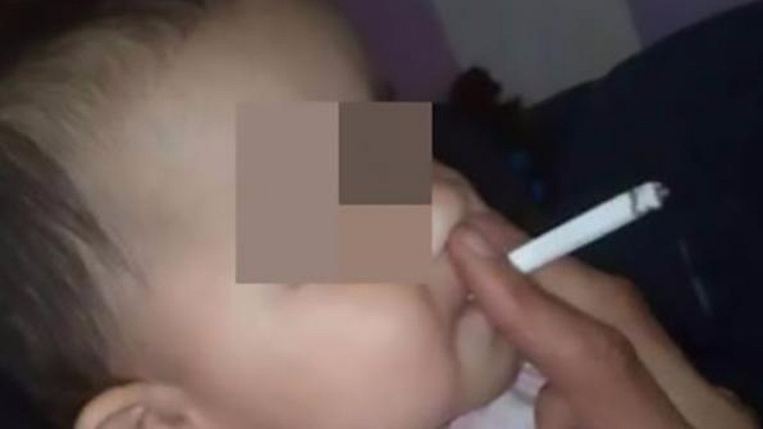 Rauchendes Baby: Ein Vater hilft seinem Kind beim Konsumieren einer Zigarette Ein Mann hilft seinem Baby beim Rauchen einer Zigarette