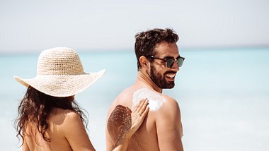 Frau cremt Rücken von Mann mit Sonnencreme ein - Foto: iStock/franckreporter