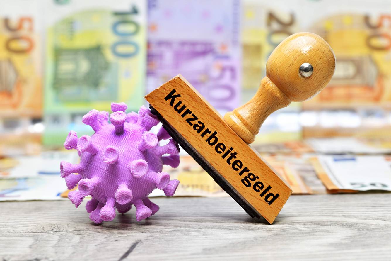 Betrug beim Kurzarbeitergeld Stempel Kurzarbeitergeld, angelehnt an ein Coronavirus, im Hintergrund Tapete aus Geldscheinen