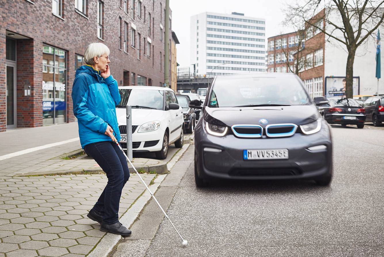 EU: Neue E-Autos müssen ab Juli Lärm erzeugen! Blinde Frau überquert Straße, auf der ein BMW i3 fährt