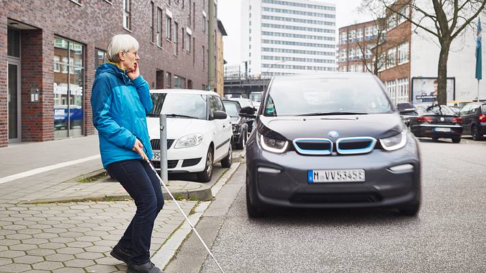 Blinde Frau überquert Straße, auf der ein BMW i3 fährt - Foto: DBSV/Schwering