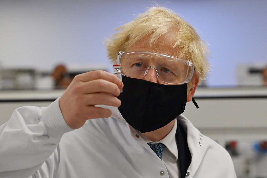 Boris Johnson mit Schutzmaske, -brille und Impfstoff