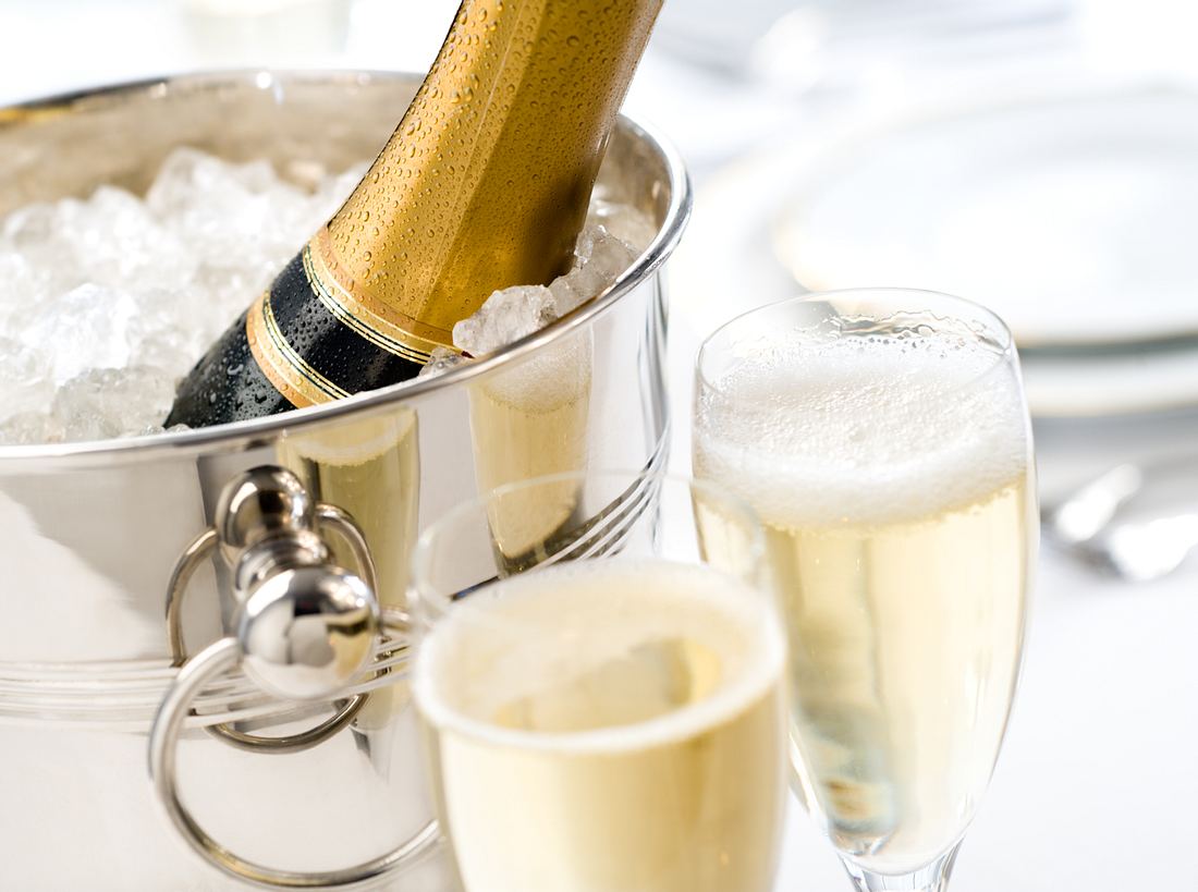Champagnerkühler im Vergleich silberner Champagnerkühler mit Crush-Eis gefüllt, Champagnerflasche und zwei gefüllte Gläser zum Anstoßen