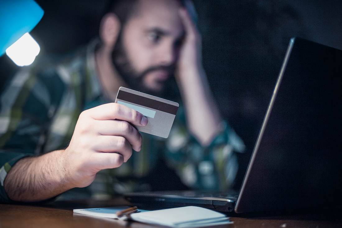 Corona-Krise: Polizei warnt vor neuem Betrüger-Trick Mann mit Bankkarte am Tisch vor seinem Laptop