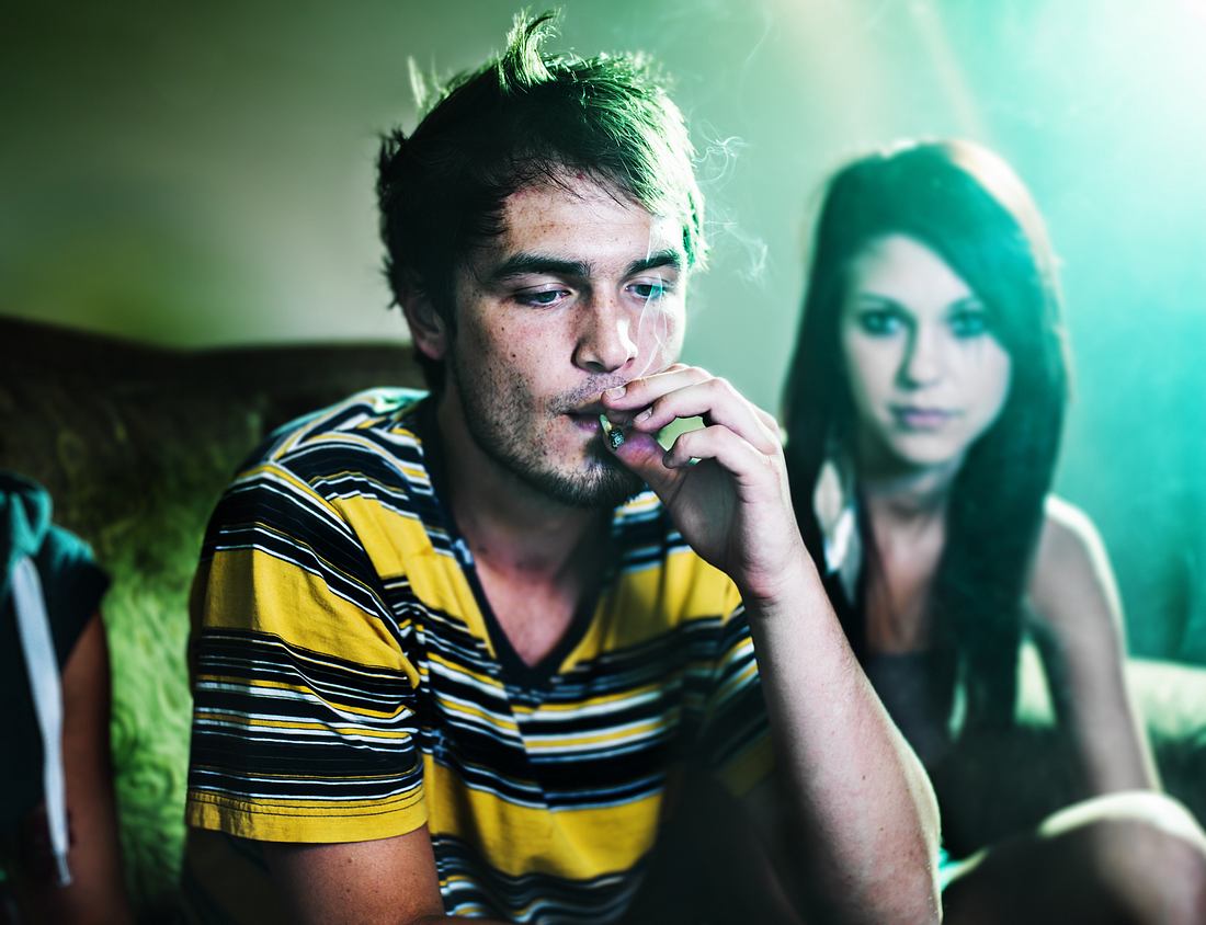 Die besten Kifferfilme fürs Fliegen mit Air Couch Junger Mann zieht an einem Joint, junge Frau im Hintergrund