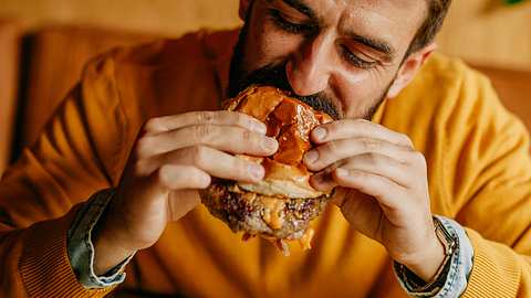 Mann beißt in Burger - Foto: iStock / Studio4