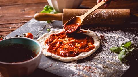 Kleine Pizza, die mit Tomatensoße bestrichen wird - Foto: iStock / oleksajewicz