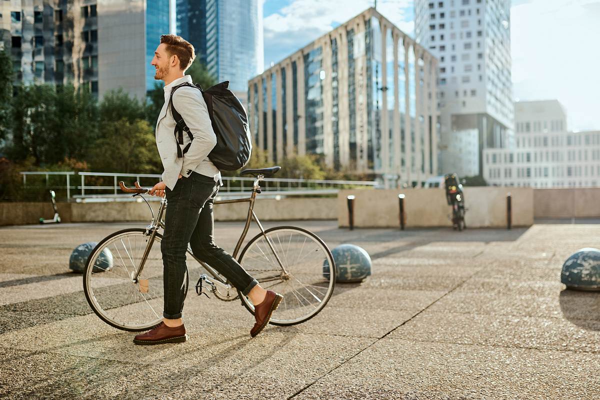 Ein Mann trägt seine Fahrradtasche als Rucksack, während er sein Rad schiebt