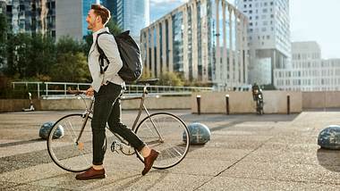 Ein Mann trägt seine Fahrradtasche als Rucksack, während er sein Rad schiebt - Foto: iStock/katleho Seisa