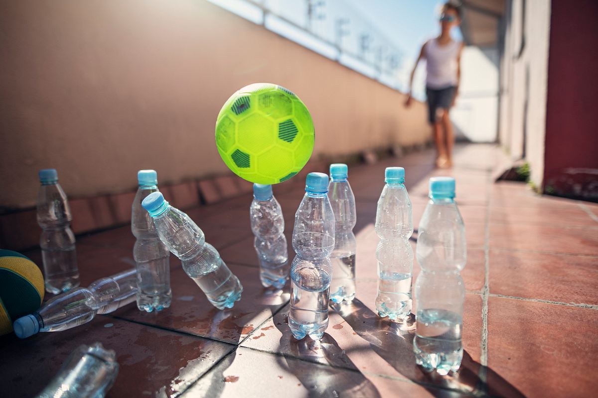 Mann schießt mit Fußball auf Flaschen