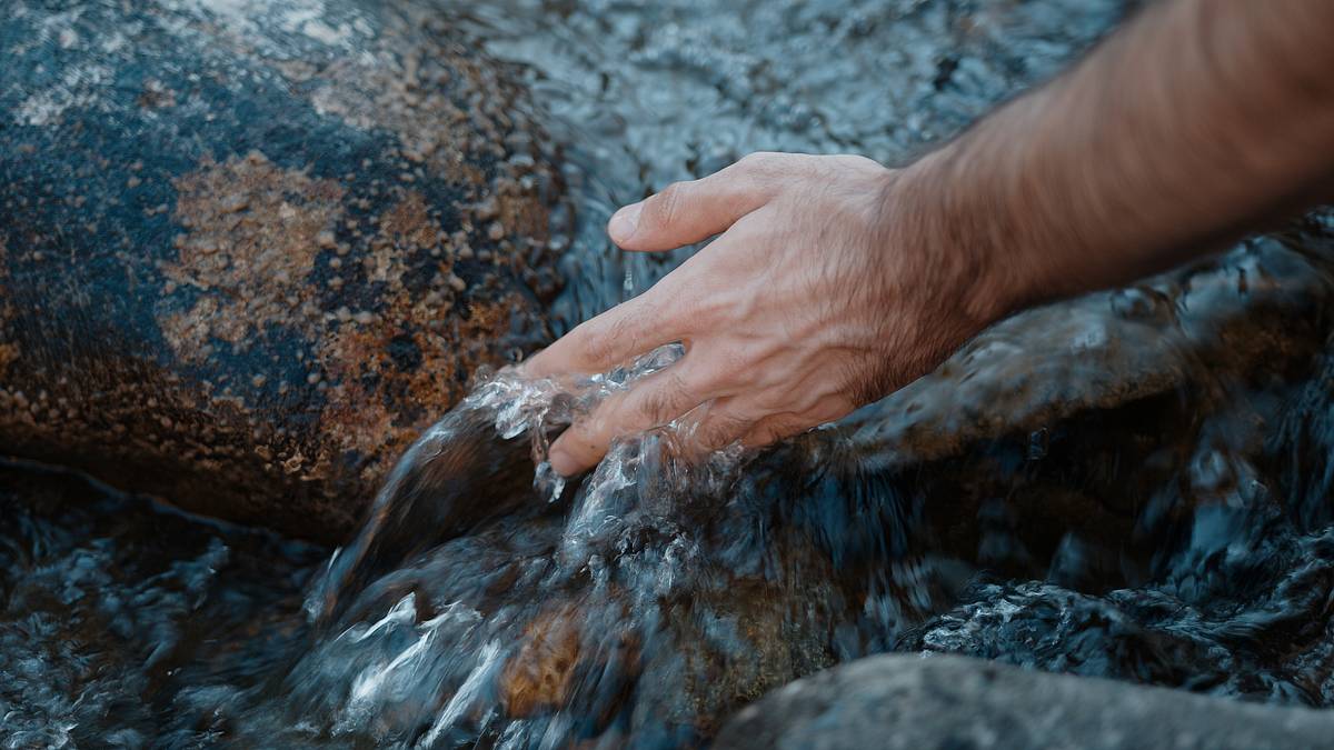 Mann steckt Hand in Flusswasser