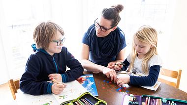 Mutter mit ihren Kindern bei den Schularbeiten Zuhause - Foto: GettyImages/Lars Baron 
