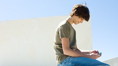 Junge spielt Mobile Game draußen auf seinem Handy  - Foto: Getty Images/PhotoAlto/Michele Constantini