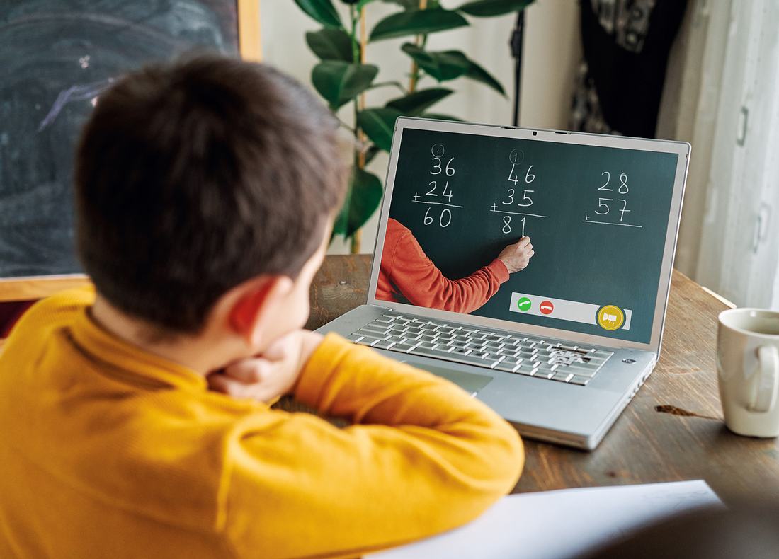 Grundschüler sitzt vor Laptop und schaut Mathe-Lehrer zu