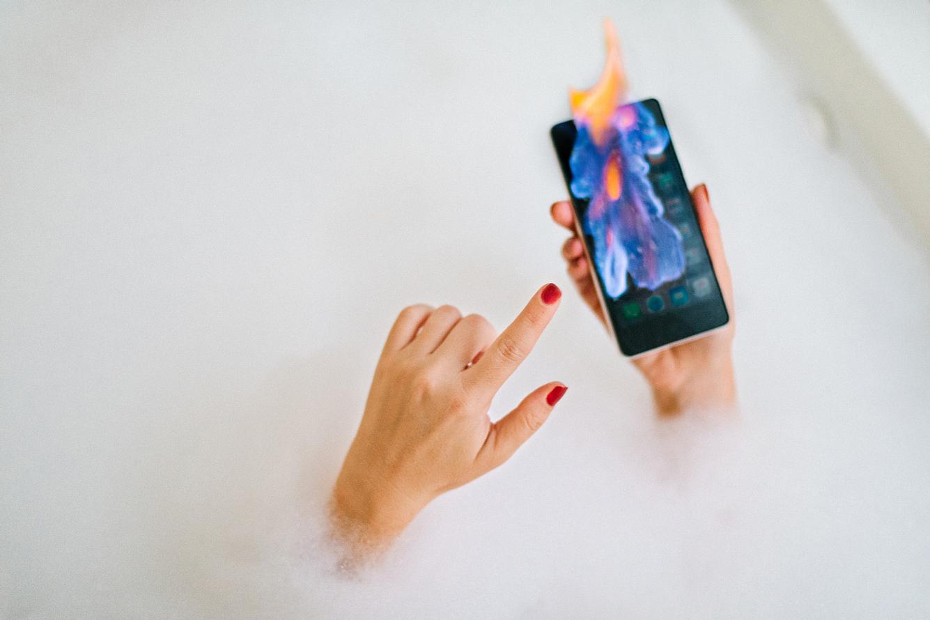 Frau in der Badewanne mit Smartphone, das in Flammen aufgeht