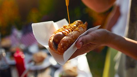 Mann macht sich Senf auf einen Hotdog - Foto: iStock / vgajic