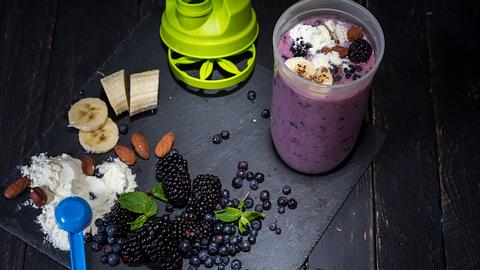 Protein Shaker, Protein Pulver und Früchte auf einem schwarzen Schieferbrett