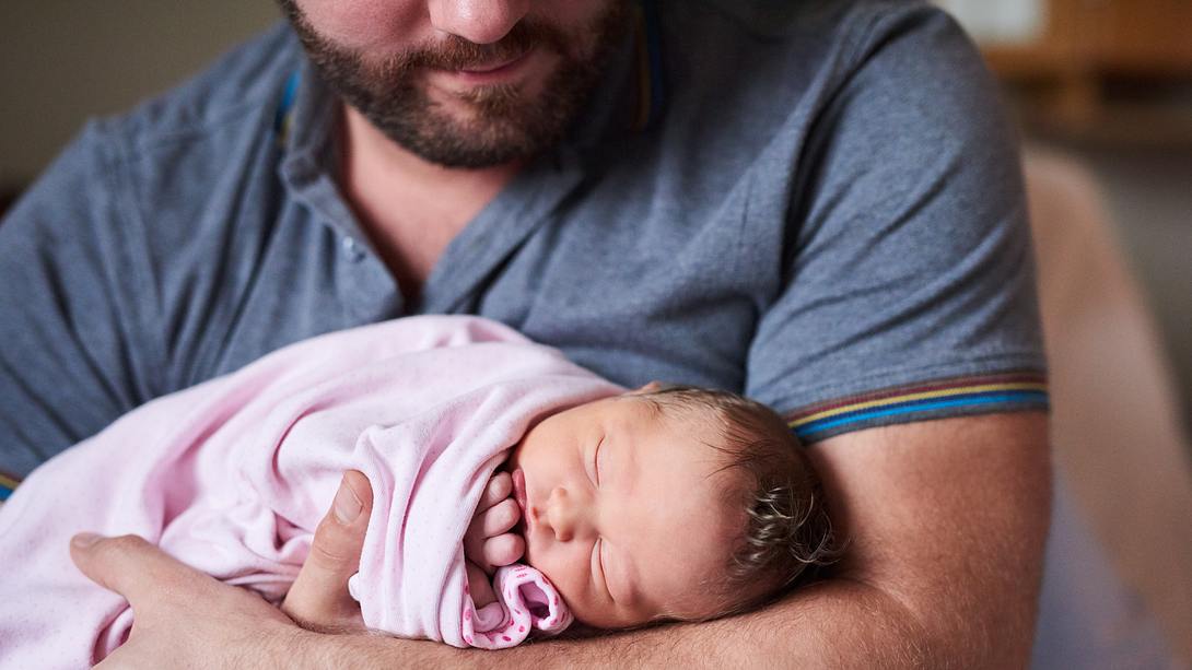 Mann mit Säugling auf Arm - Foto: iStock/Yuri_Arcurs