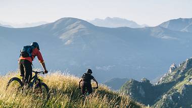 Mountain bikers ride down grassy mountain ridge - Foto: iStock / AscentXmedia