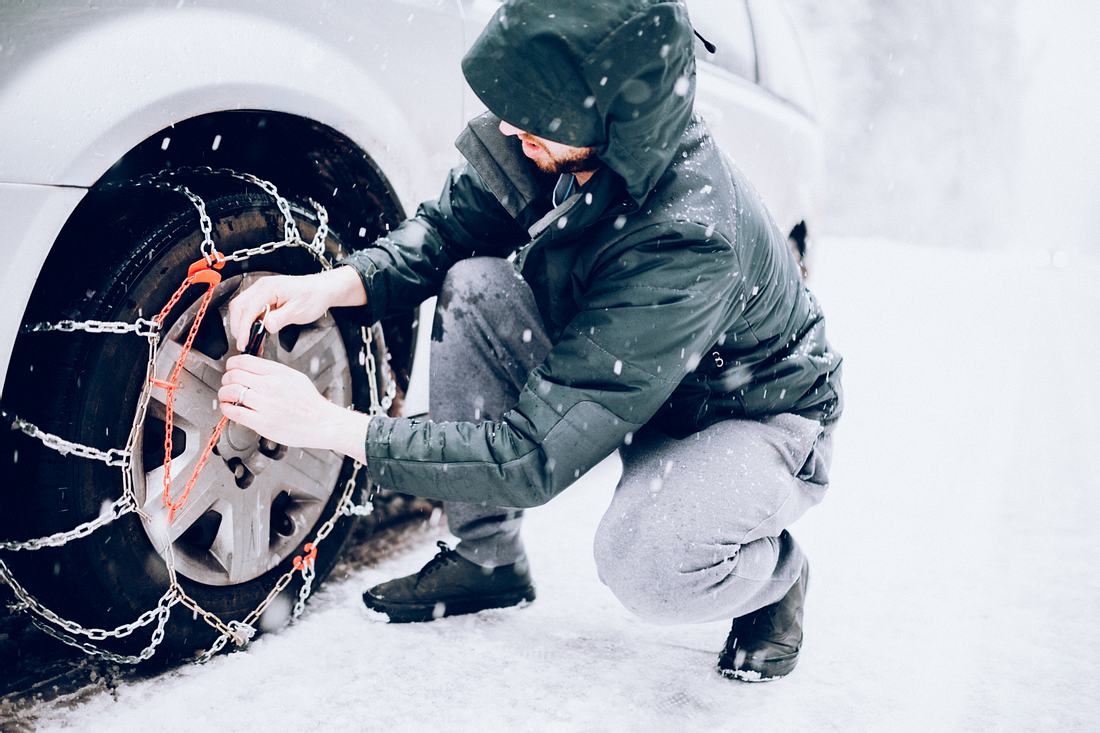 Schneeketten kaufen Mann legt Schneeketten an