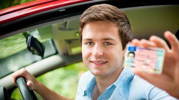 Junger Mann zeigt freudestrahlend seinen Führerschein - Foto: iStock / AlexRaths