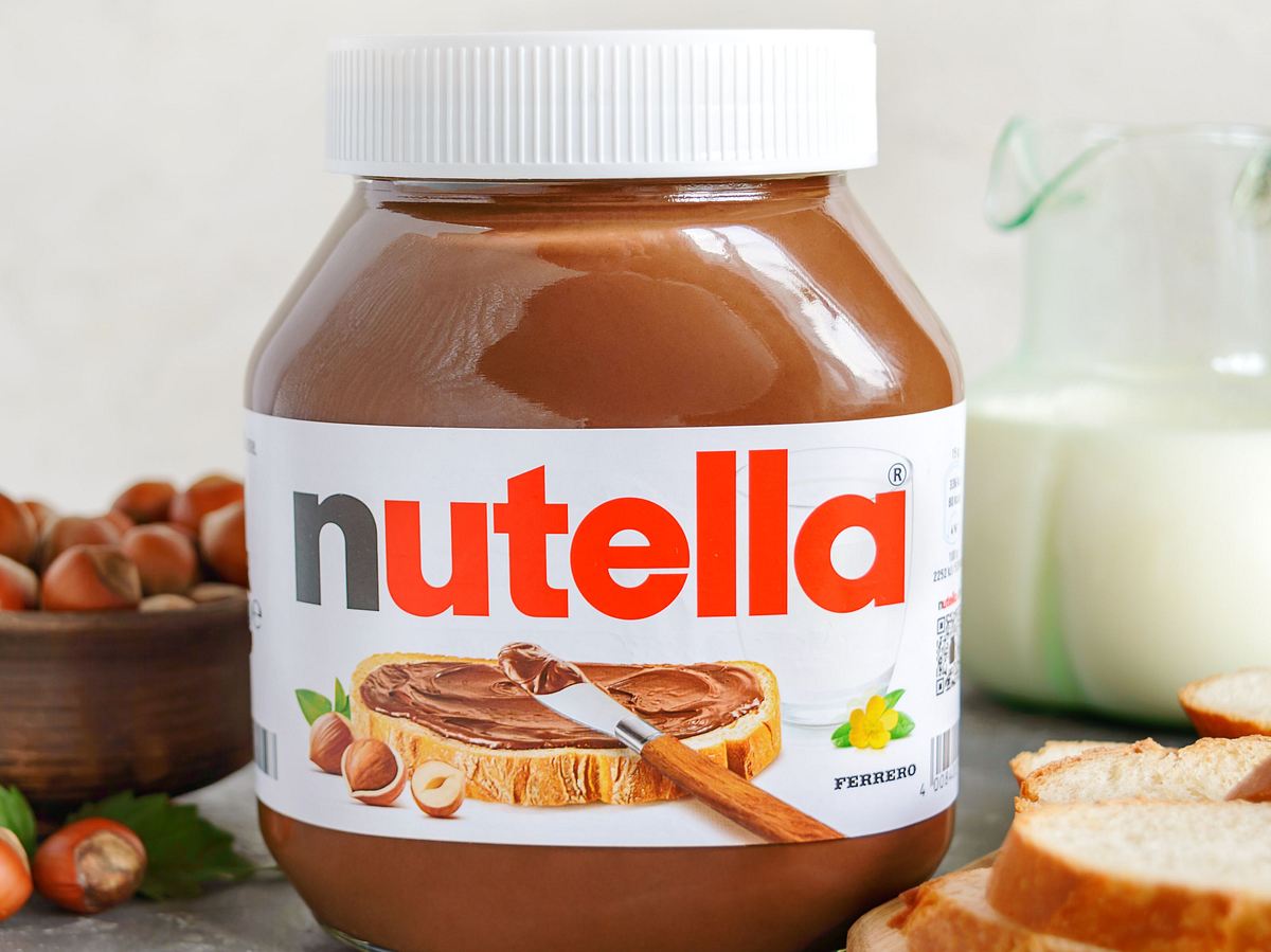 Nutella-Glas, daneben Haselnüsse, Milch und Brotscheiben