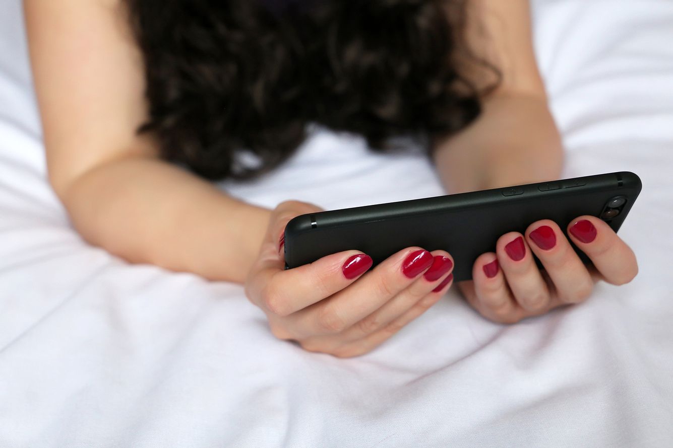 Frau guckt in ihr Handy auf dem Bett