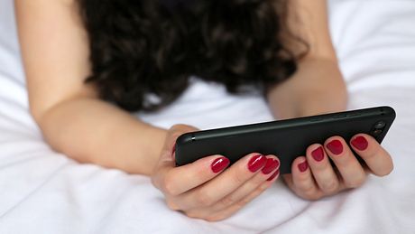 Frau guckt in ihr Handy auf dem Bett - Foto: iStock/Oleg Elkov