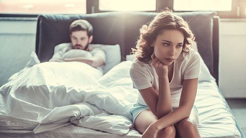 Mann liegt traurig im Bett, Frau sitzt auf der Bettkante und guckt genervt - Foto: iStock/vadimguzhva