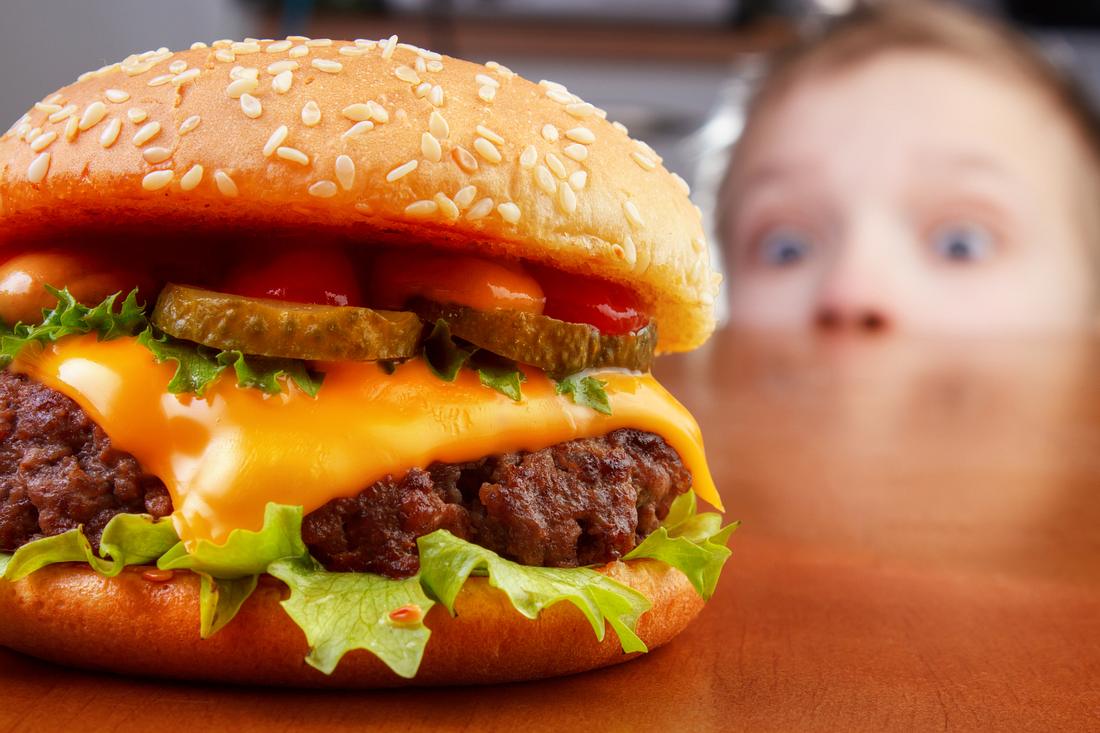 Kind schaut gierig auf einen Cheeseburger