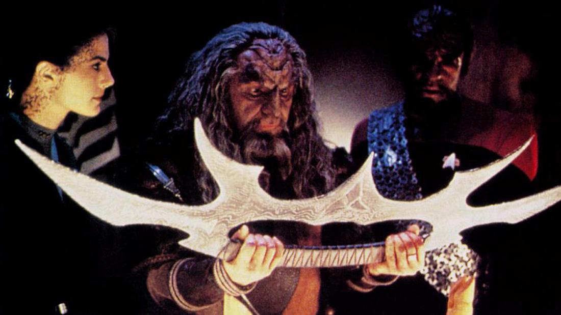 Ein Klingone Kor hält ein Bat‘leth in seinen Händen. Der Klingone Kor hält das Bat‘leth des Klingonen-Oberhaupts Kahless in seinen Händen.