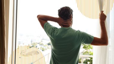 Mann steht vor Fenster und zieht Vorhang auf  - Foto: iStock / GlobalStock
