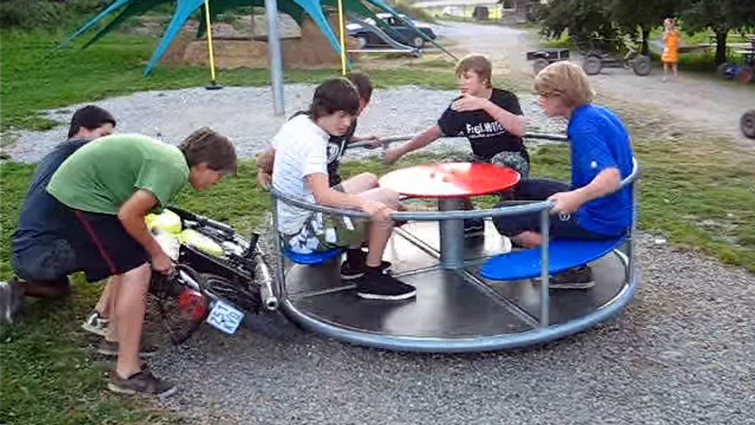 Jugendliche halten ein Moped-Rad an an Spielplatz-Karussell