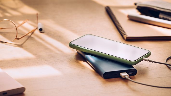 Handy und Power Bank liegen auf einem Schreibtisch aus Holz - Foto: iStock/FreshSplash