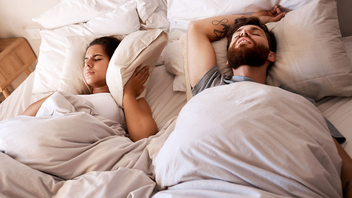 Mann und Frau im Bett, Frau hält sich Kissen über die Ohren