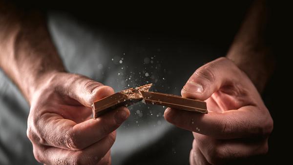 Mann bricht Schokoriegel durch - Foto: iStock / Anna Makarenkova