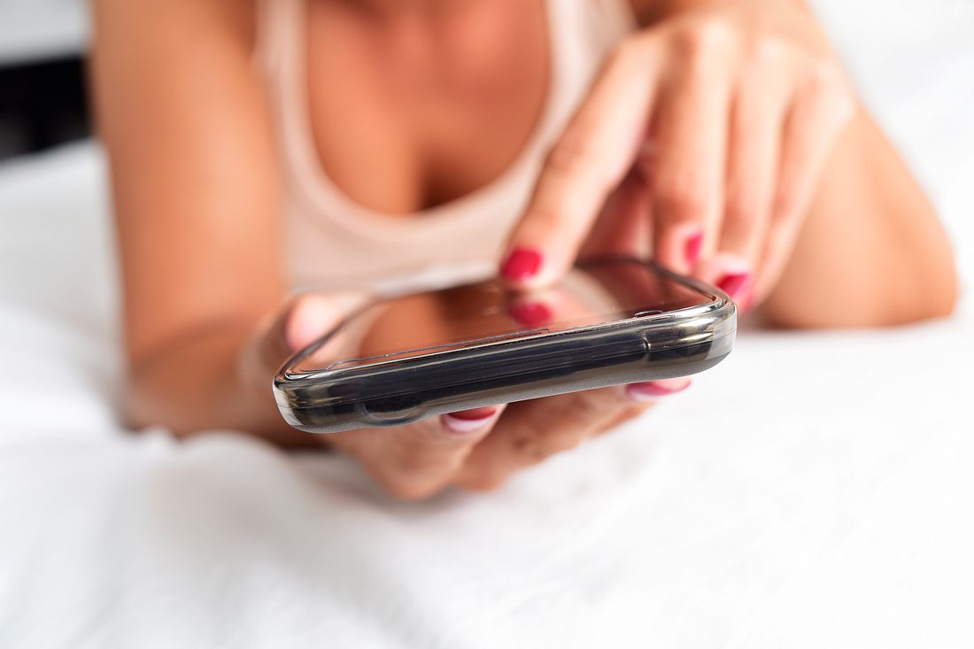 Sex in Corona-Zeiten: So funktioniert Sexting Frau liegt im Bett und hält ein Smartphone in der Hand