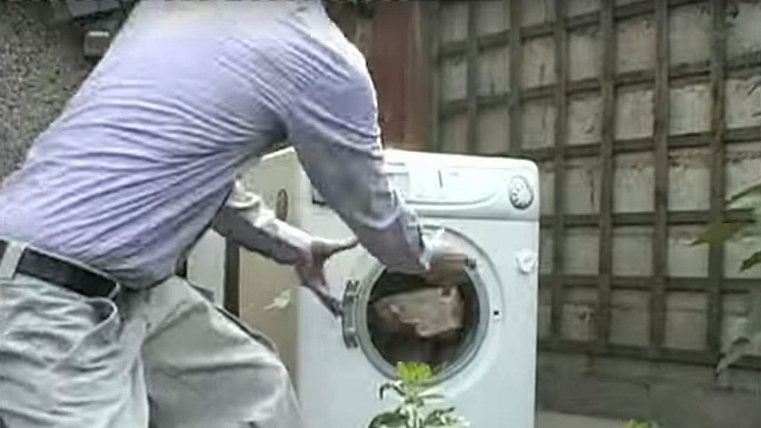 Ein Mann wirft einen Ziegelstein in eine Waschmaschine