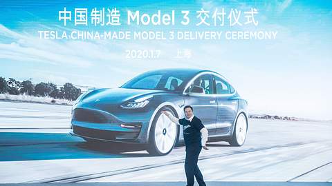 Elon Musk auf Bühne vor Bild eines Tesla Model-3 - Foto: imago images / Xinhua