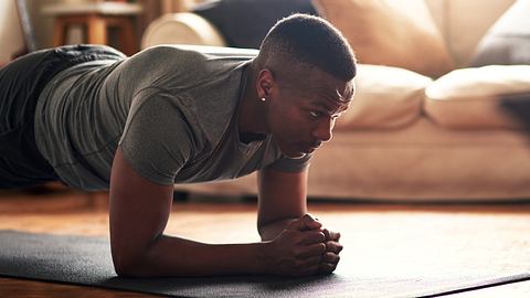 Junger Mann steht in Planke auf seiner Trainingsmatte zuhause - Foto: iStock/PeopleImages