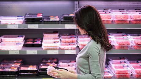 Frau steht vor dem Fleischregal im Supermarkt - Foto: iStock / Natissima