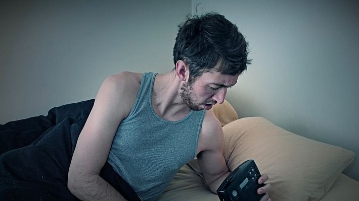 Mann im Bett mit Wecker - Foto: iStock/RyanJLane